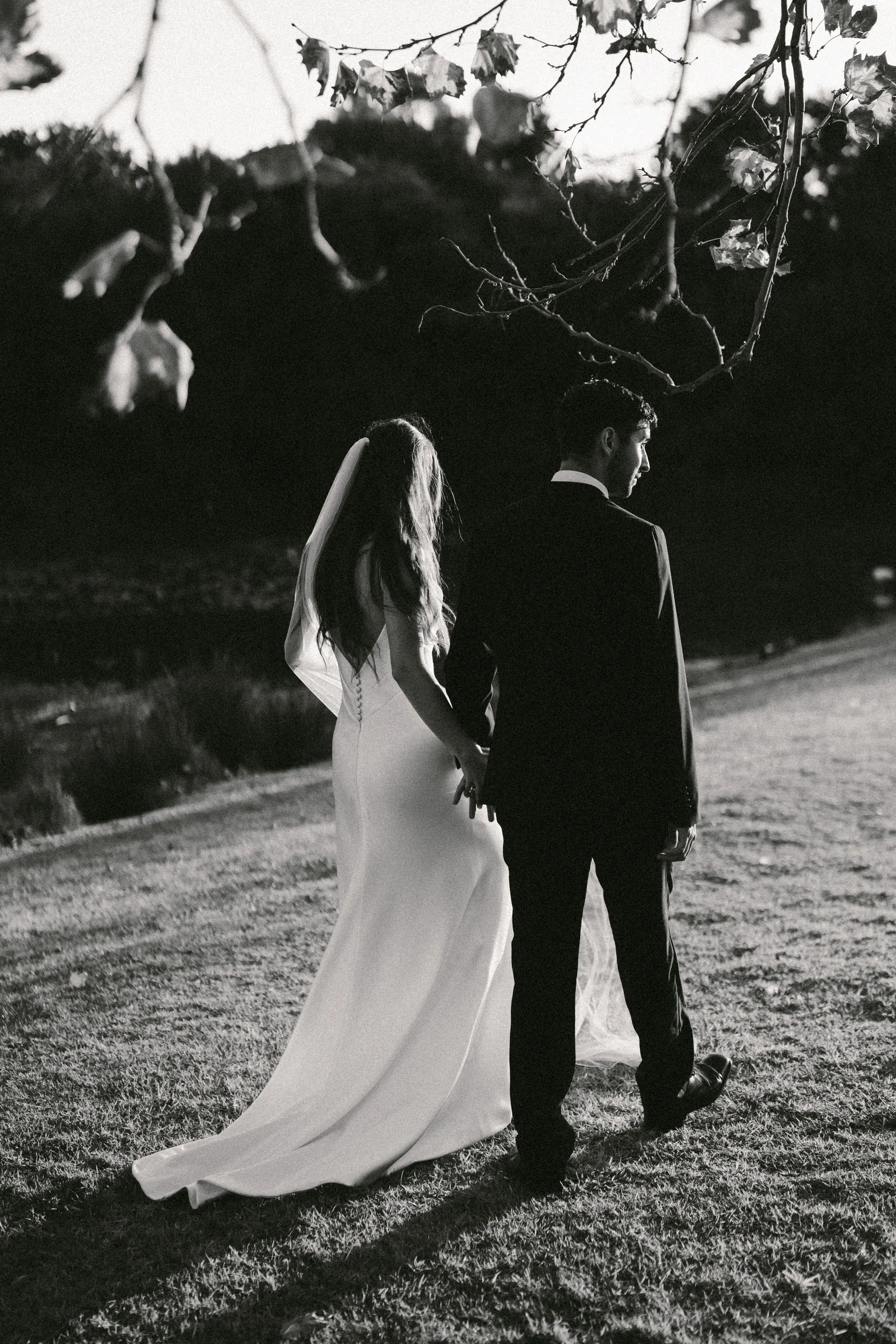 A bride and groom walking away across a lawn at dusk, in black and white.