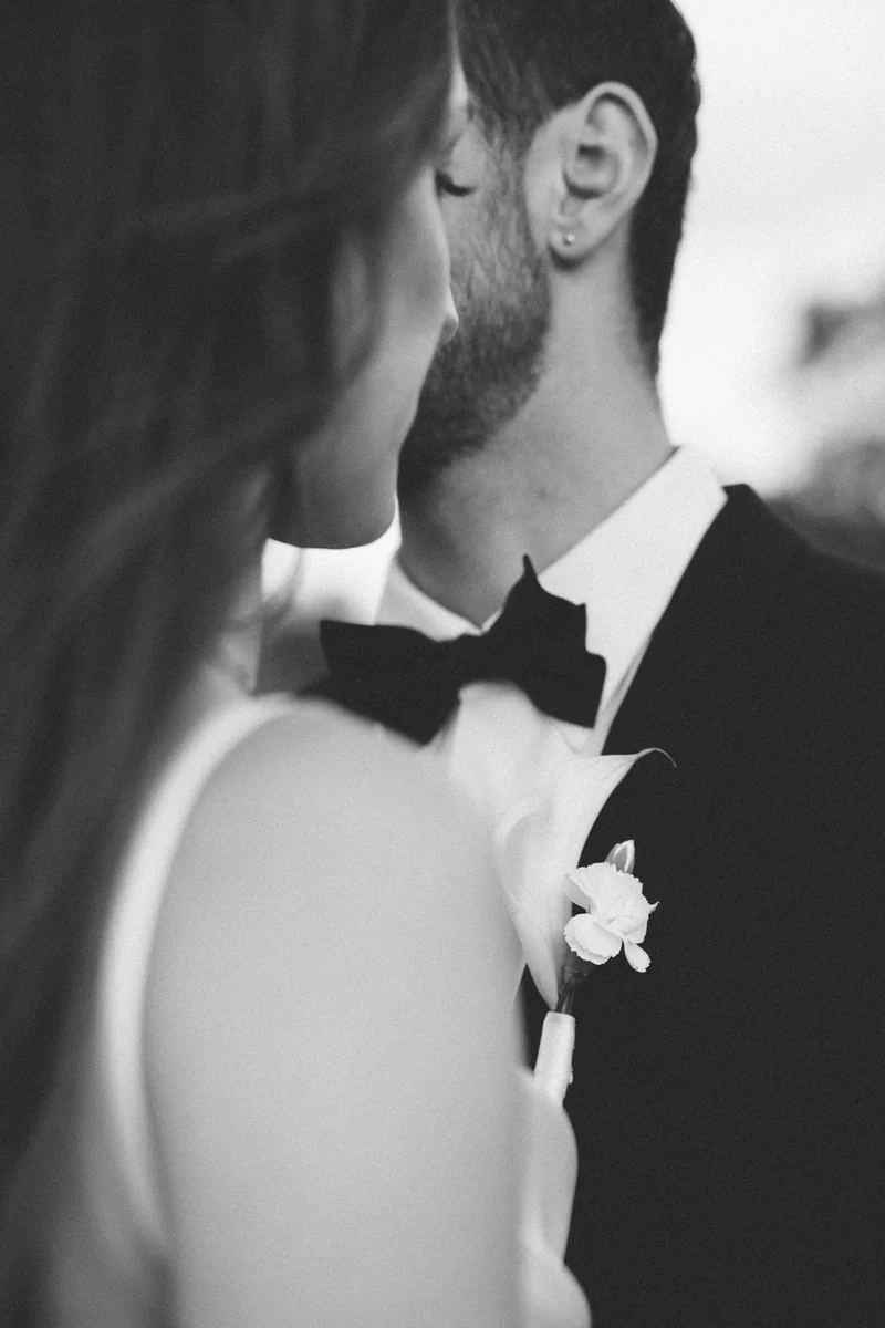 A bride and groom standing close, his boutonniere between them