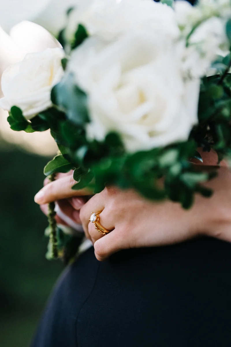 A hand with a gold wedding ring resting on white roses